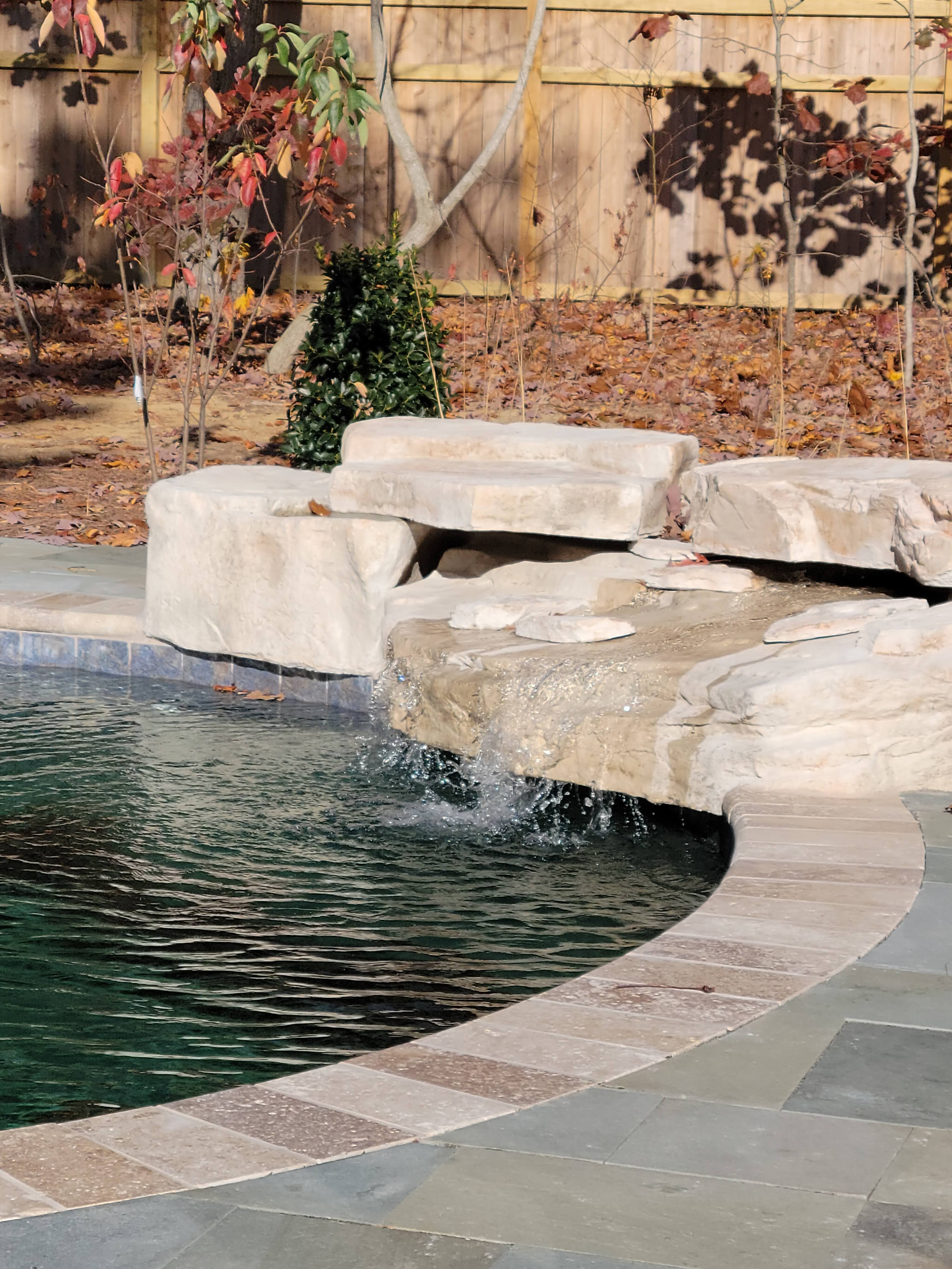 Natural stone waterfall feature with flagstone pool deck